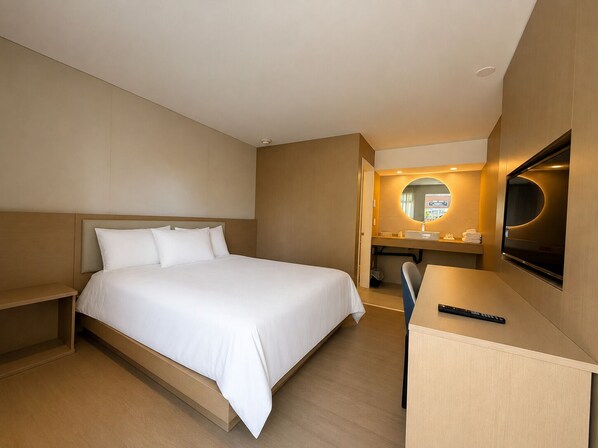 A hotel room with a bed, a desk, a chair, a TV, and a bathroom with a mirror and sink. - Motel La Siesta (Longueuil)