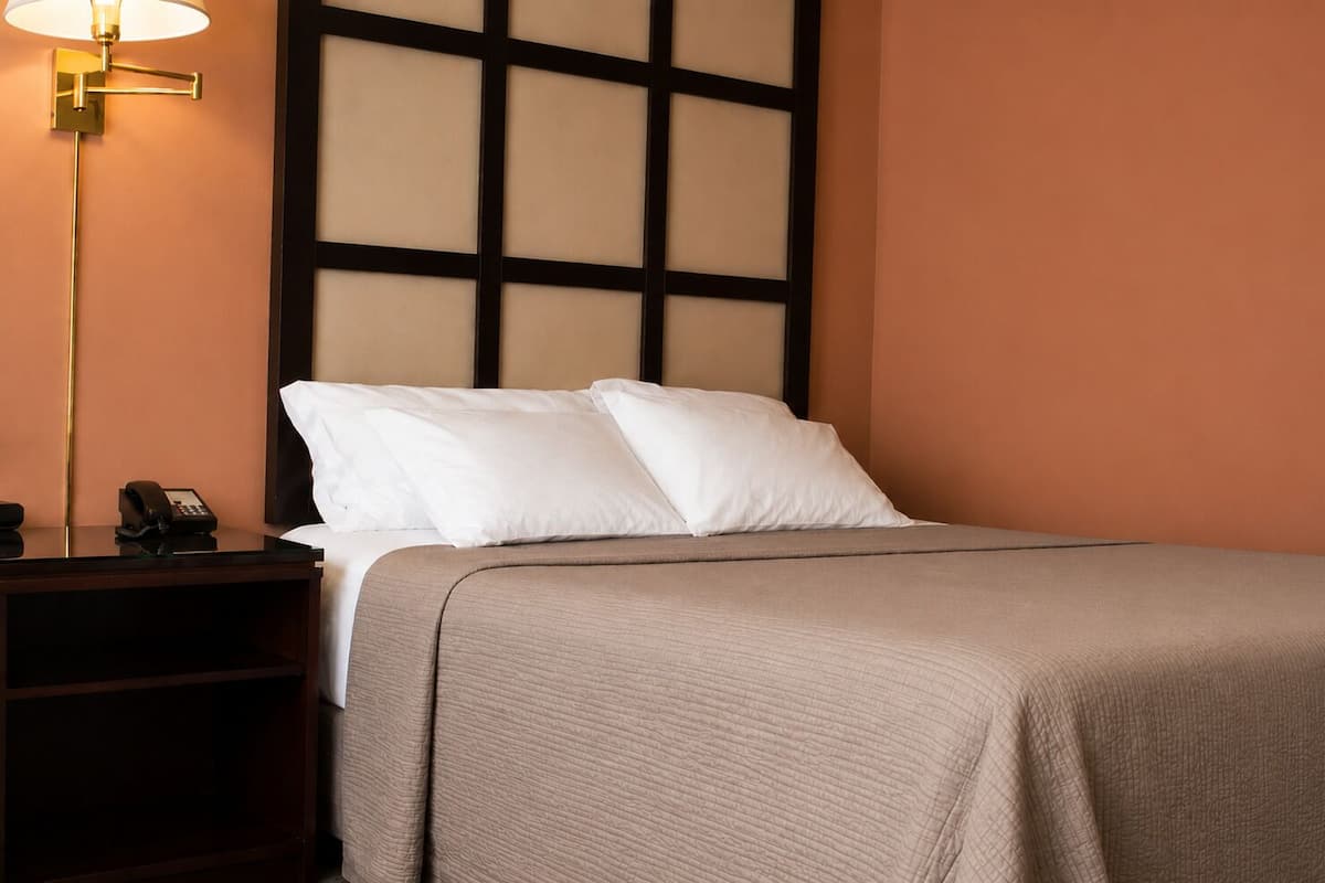 A hotel room with a bed, a nightstand with a phone, and a wall with a grid pattern.