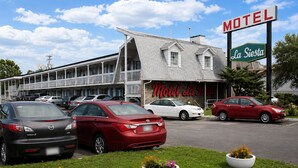 Un motel con un letrero que dice 'Motel La Siesta', que presenta un edificio de dos pisos con techo inclinado y área de estacionamiento techada.