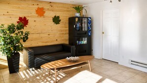 Un salón moderno con pared de madera, un sofá negro, una mesa de centro de madera y un mueble de entretenimiento negro con una planta encima.