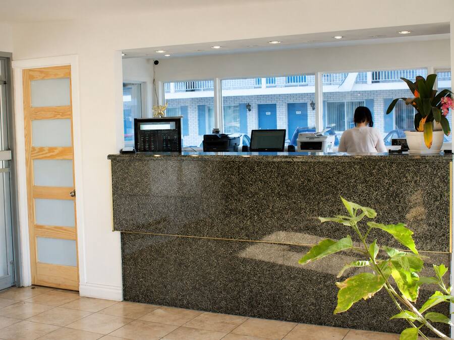 A reception desk with a computer, a phone, and a printer. There is a window with a view of a building outside.