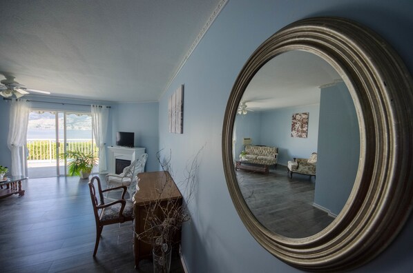 A living room with a fireplace, a large mirror, and a view of the outdoors. - OK Whistle Stop Bed & Breakfast (Penticton)
