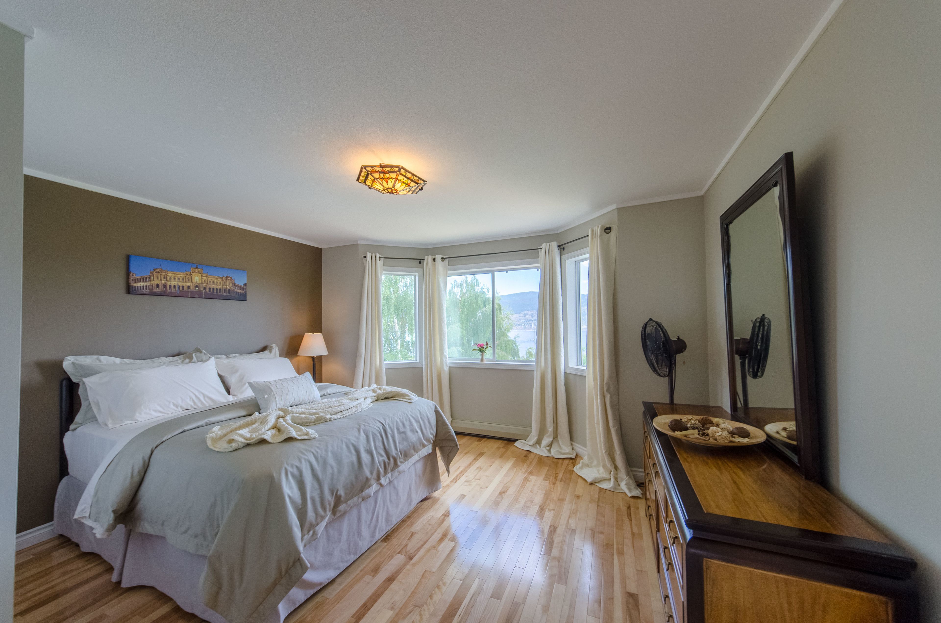 A bedroom with a bed, a nightstand, a dresser, a mirror, and a window with curtains.