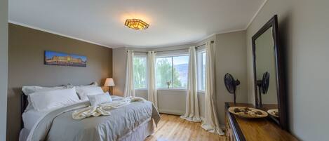 A bedroom with a bed, a nightstand, a dresser, a mirror, and a window with curtains.