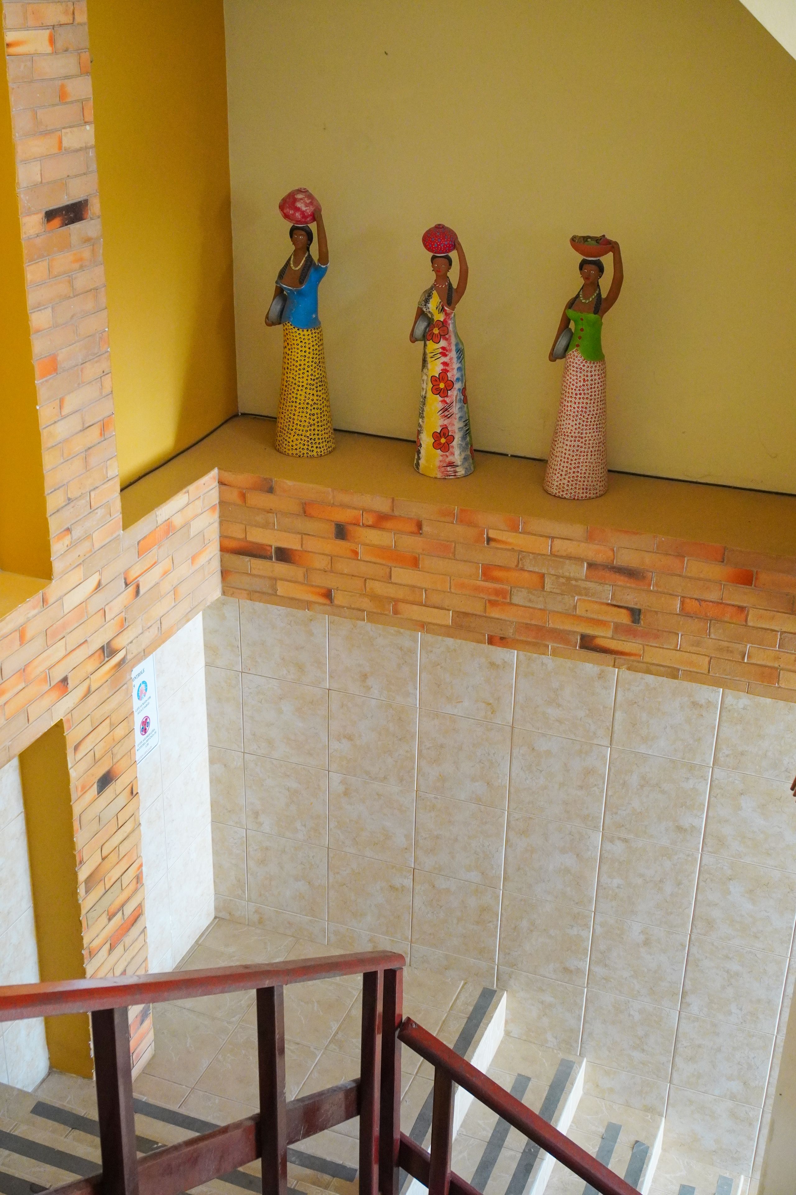 Uma escadaria com corrimão leva a um patamar onde três figuras decorativas estão colocadas em um pedestal.