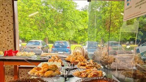 A bakery display with various baked goods and a view of parked cars and trees outside. - Pousada Jardins do Porto (Ipojuca)