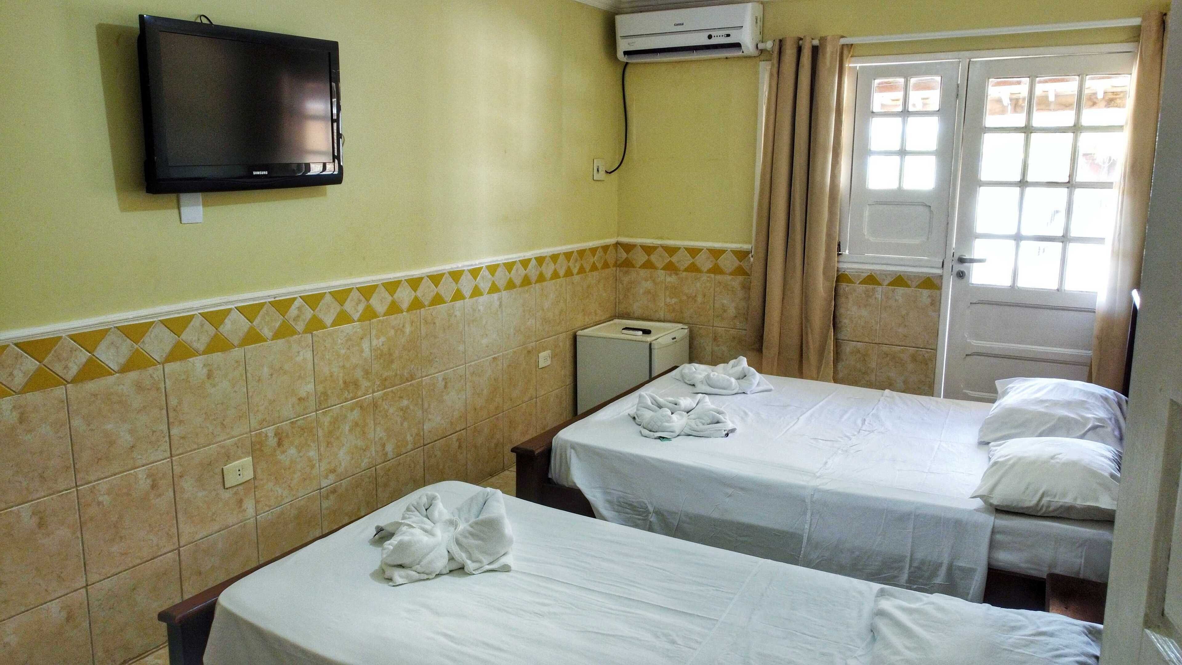 Habitación de hotel con dos camas, televisión, aire acondicionado y ventana con cortinas.