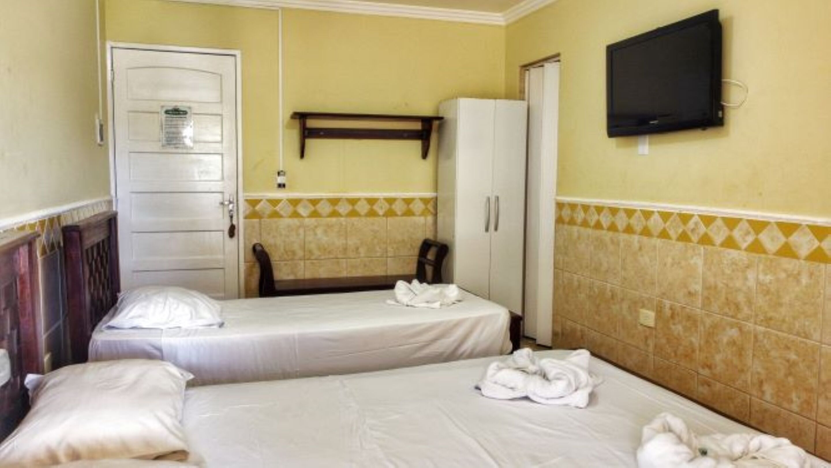 Habitación de hotel con dos camas, un armario, un televisor y la puerta del baño.