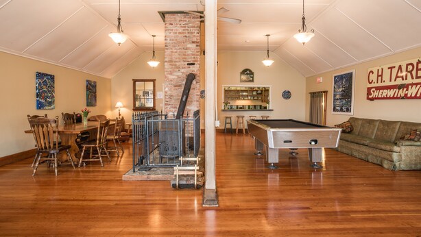 Une pièce spacieuse équipée d’une table de billard, de chaises en bois, d’une cheminée en briques et d’un coin bar.