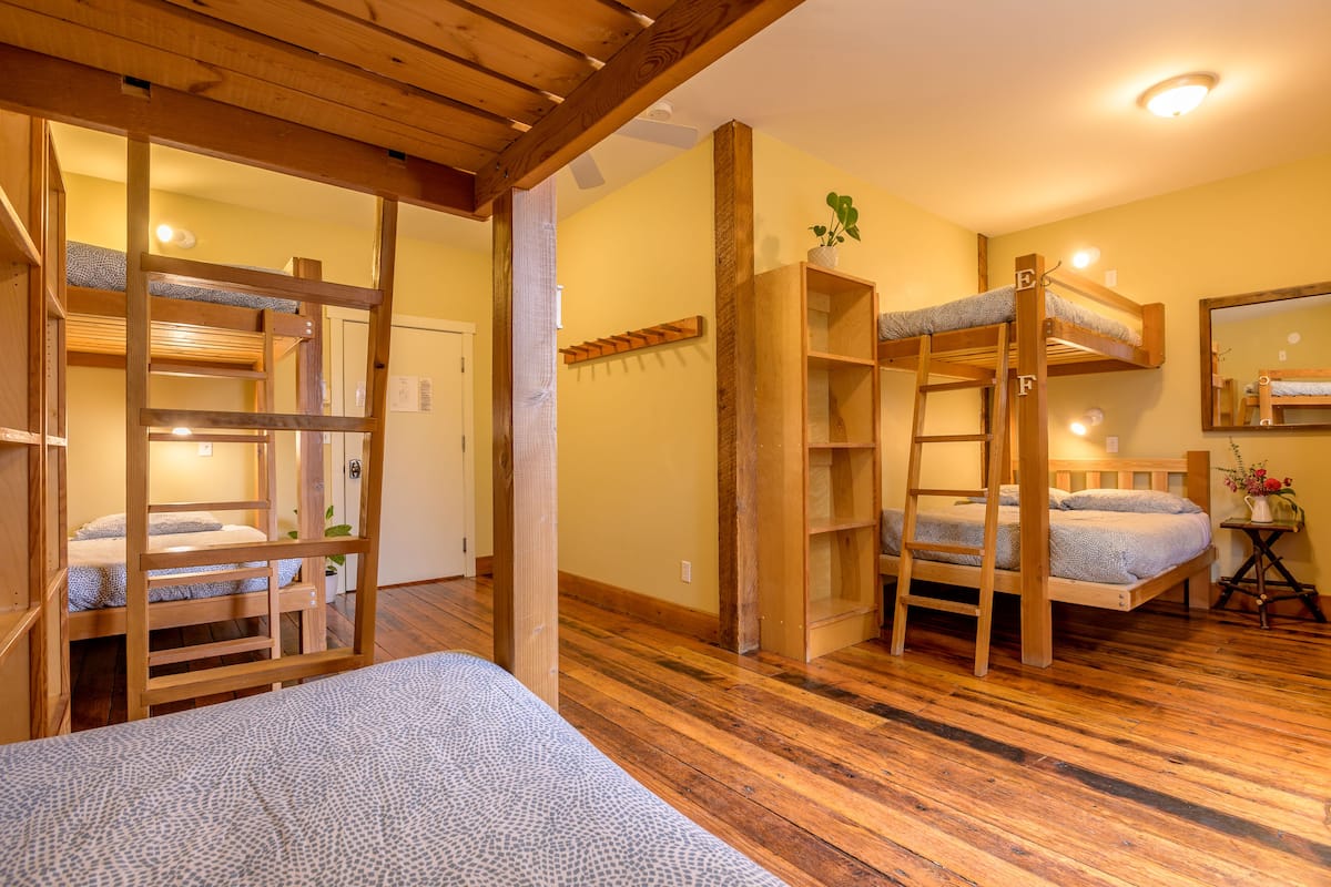 A room with bunk beds, wooden beams, and a small shelf with a plant.