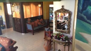 A living room with a sofa, a table with a vase of flowers, a large mirror, and a wall with a painting. - Green House Aparta Hotel (Santo Domingo)