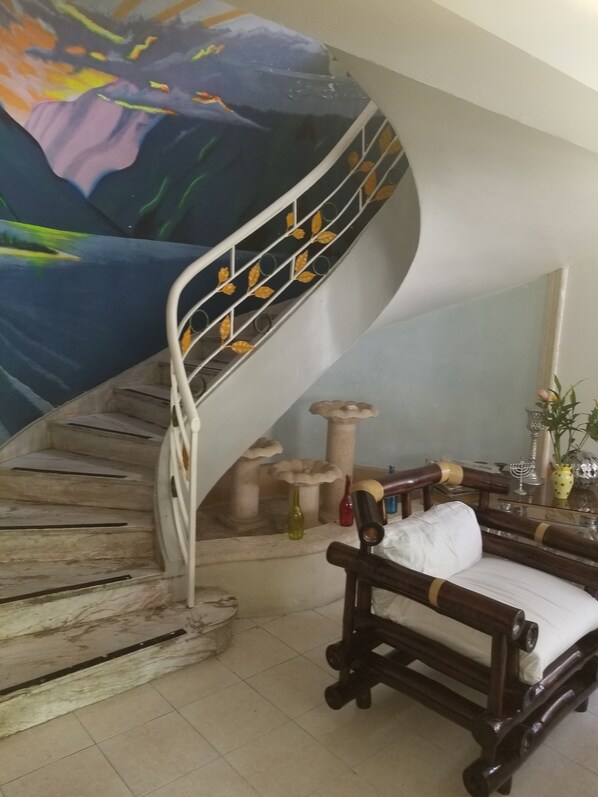 A spiral staircase with a mural, a wooden bench, and a dining table with glassware.