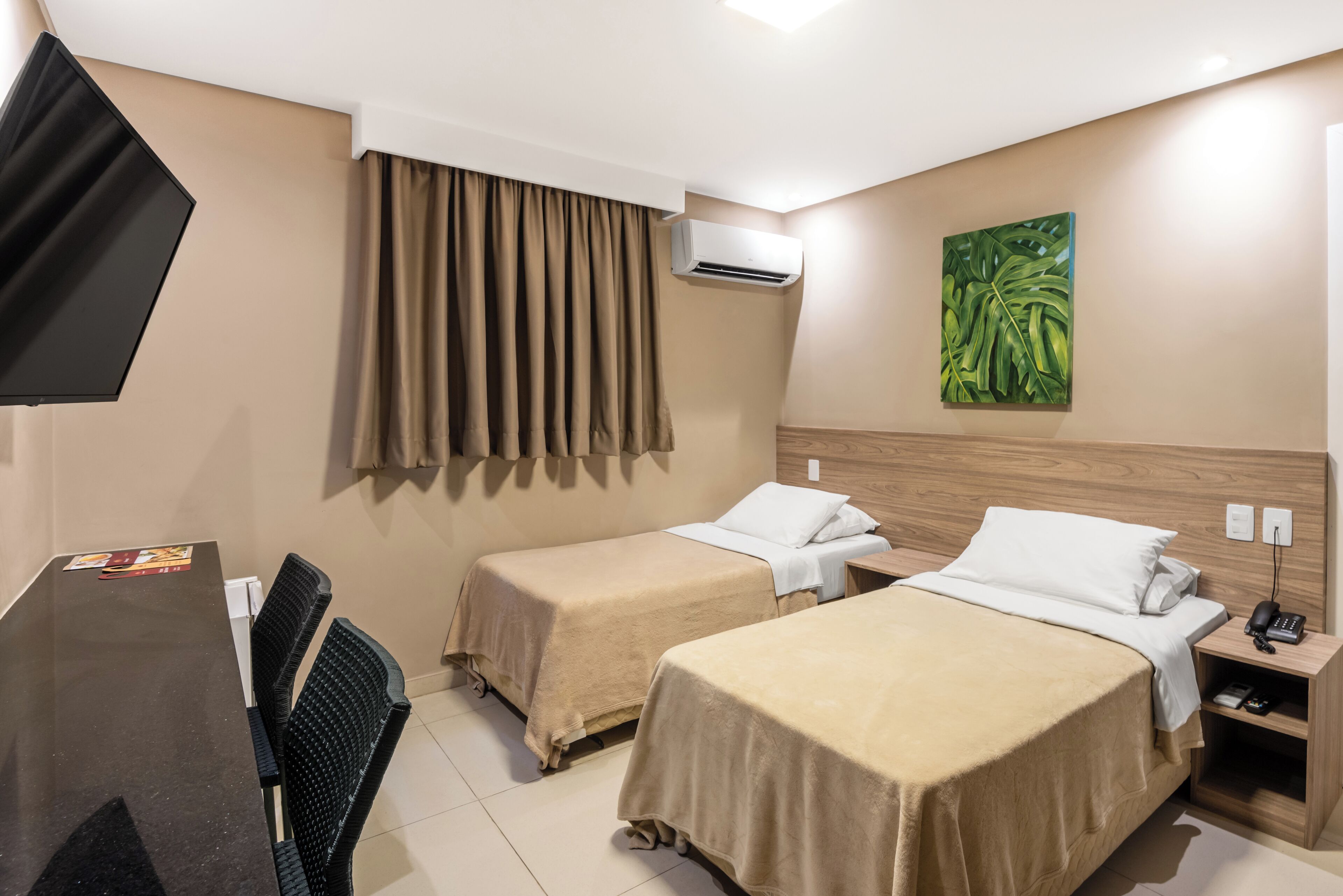 Habitación de hotel con dos camas, un escritorio con silla, aire acondicionado, un cuadro en la pared y un teléfono en la mesita de noche.