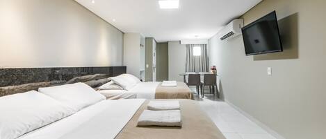 A hotel room with two beds, a TV mounted on the wall, and a desk with chairs.