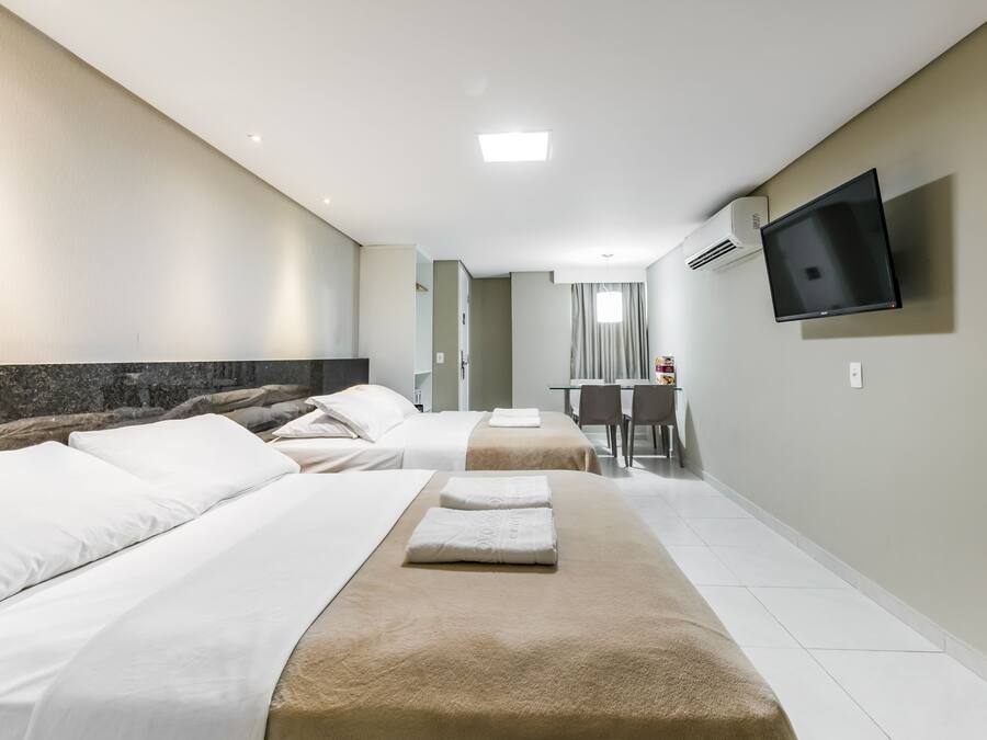 Habitación de hotel con dos camas, un televisor montado en la pared y un escritorio con sillas.