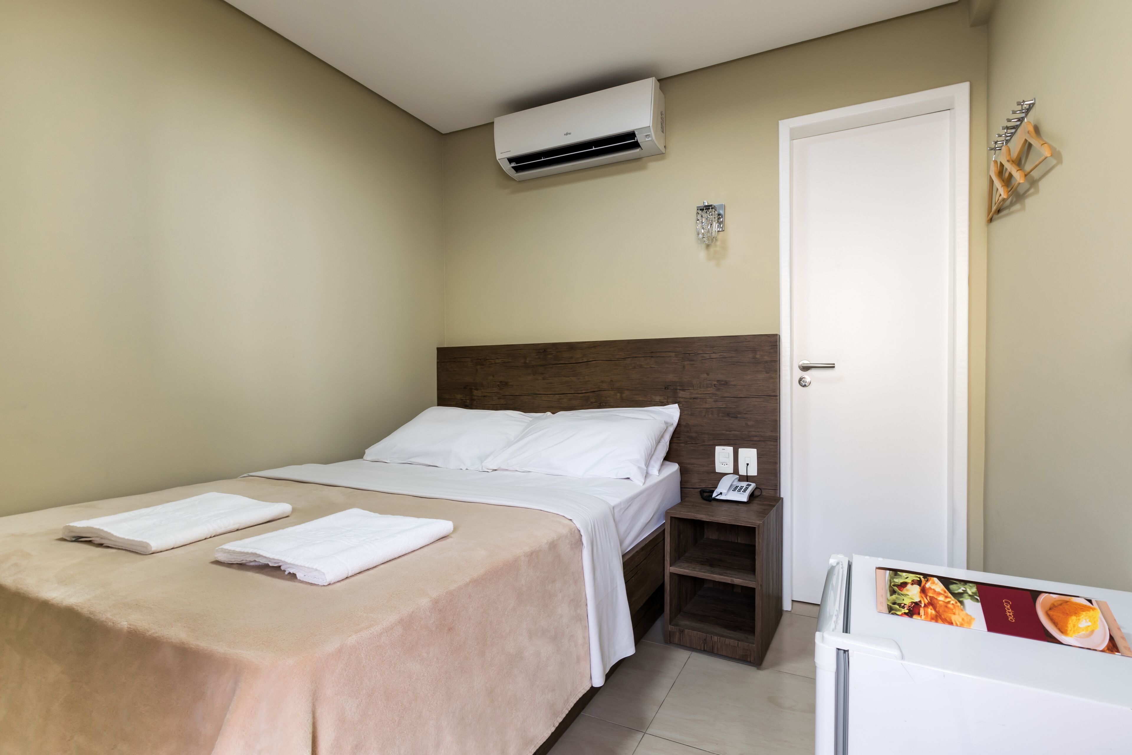 Ein ordentlich eingerichtetes Hotelzimmer mit Bett, Nachttisch und Klimaanlage.