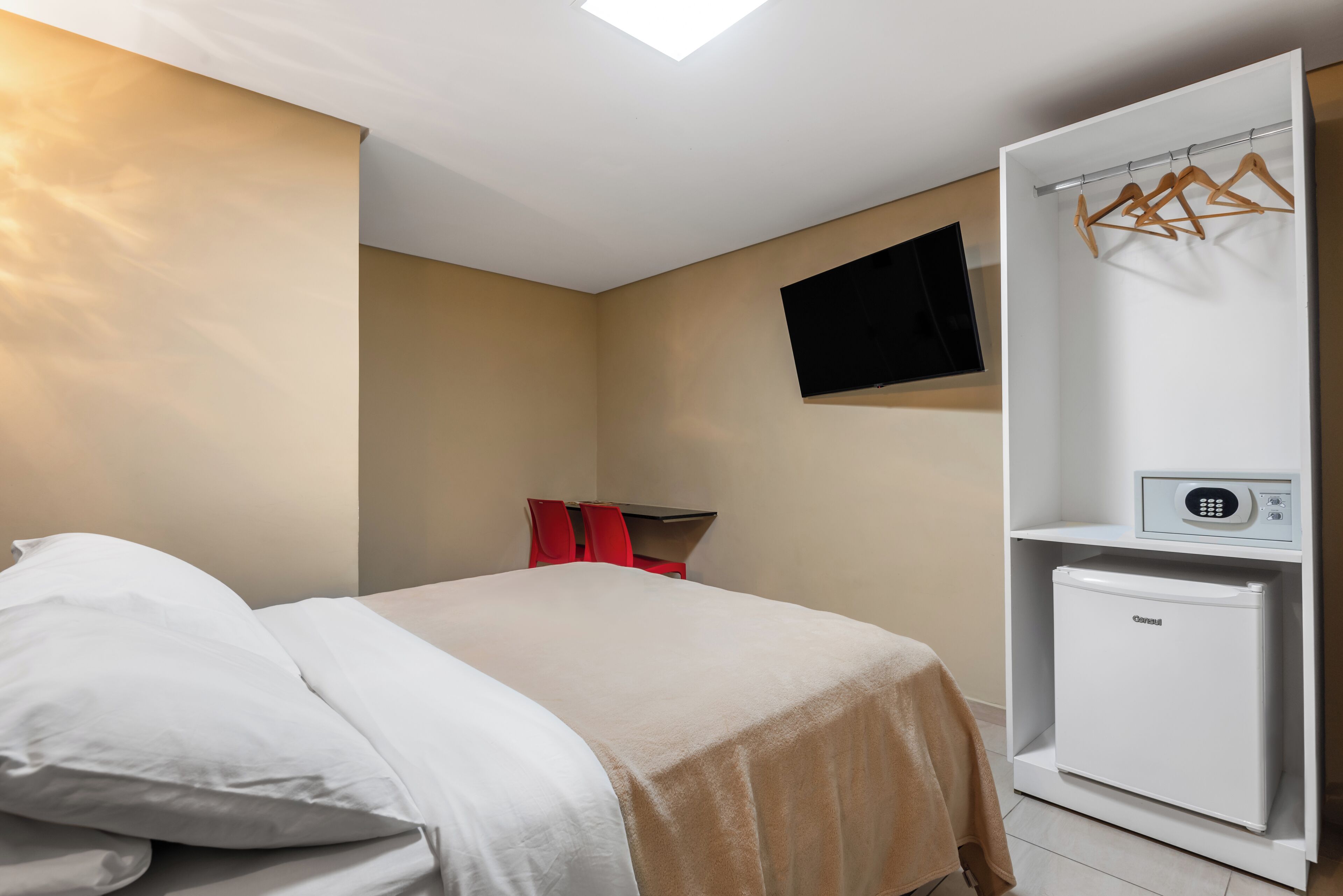 Habitación de hotel con cama, refrigerador pequeño, televisor montado en la pared y armario con perchero.
