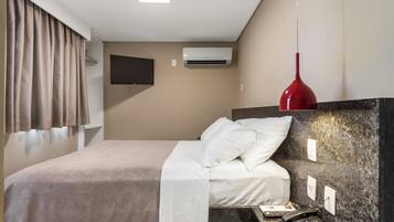 Quarto de hotel com cama, televisão na parede, aparelho de ar condicionado, telefone e luminária pendente vermelha.