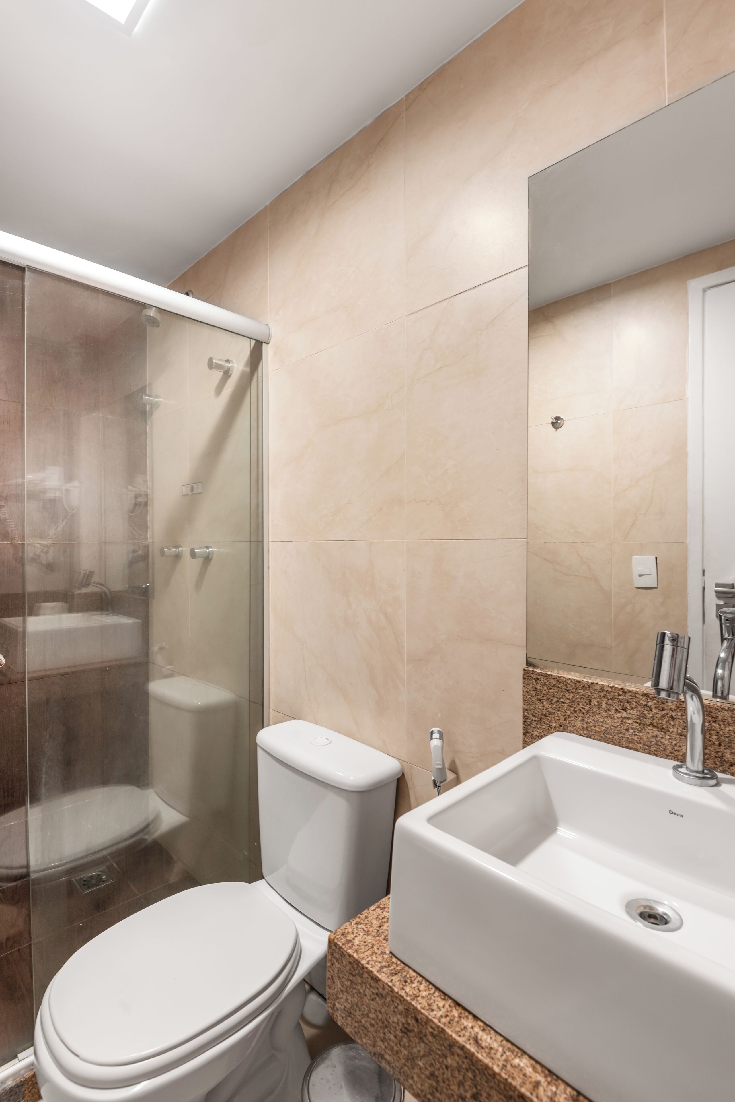 Un baño moderno con ducha acristalada, inodoro blanco y lavamanos sobre encimera de granito.