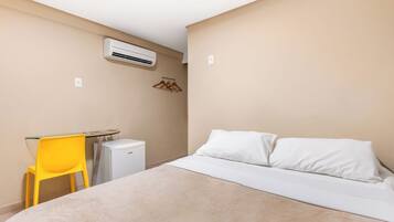 Hotellihuoneessa on sänky, pieni pöytä, keltainen tuoli, valkoinen ilmastointilaite ja seinään kiinnitetty lämmitin.
