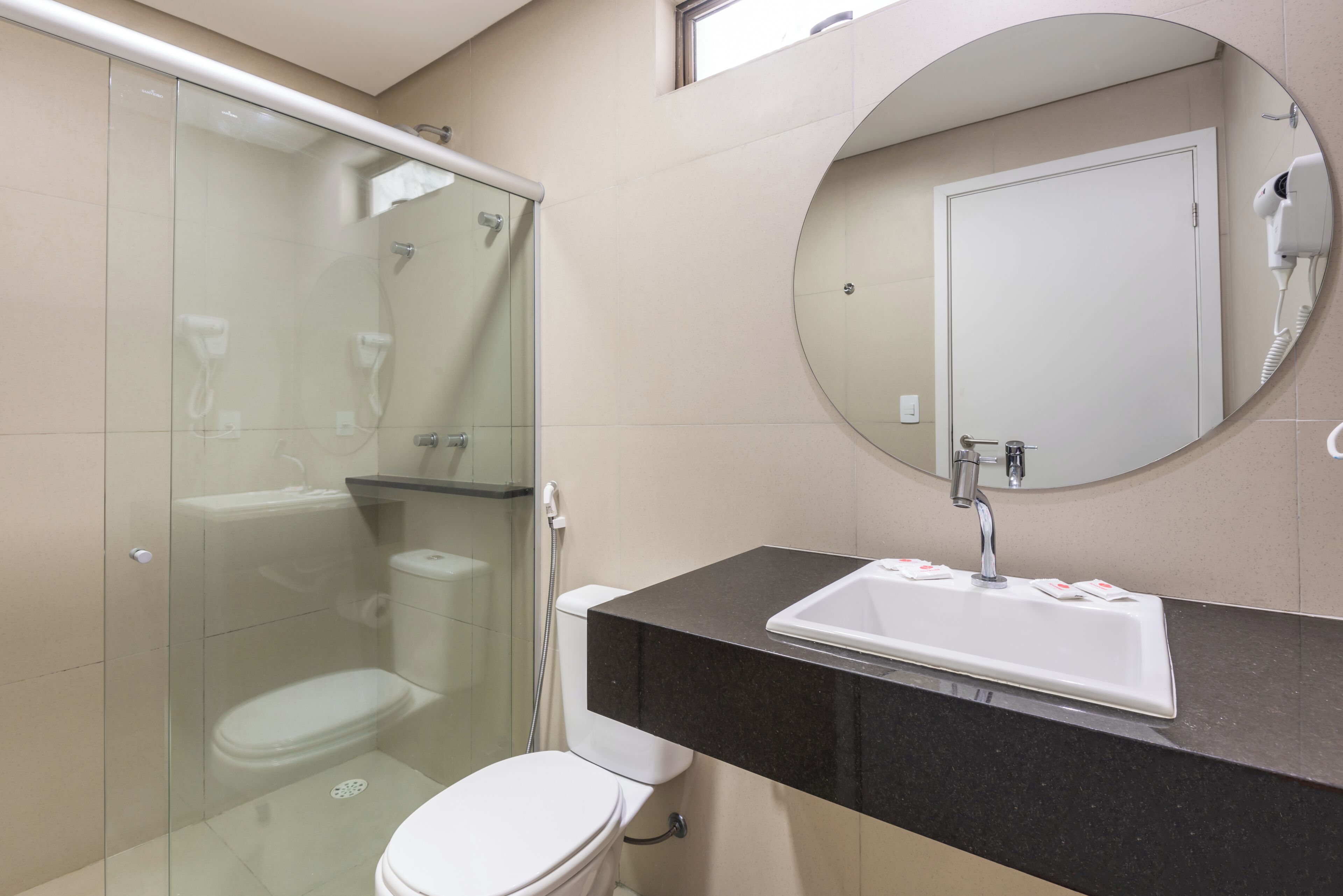 A modern bathroom with a glass-enclosed shower, a white toilet, a black countertop with a sink, and a round mirror.