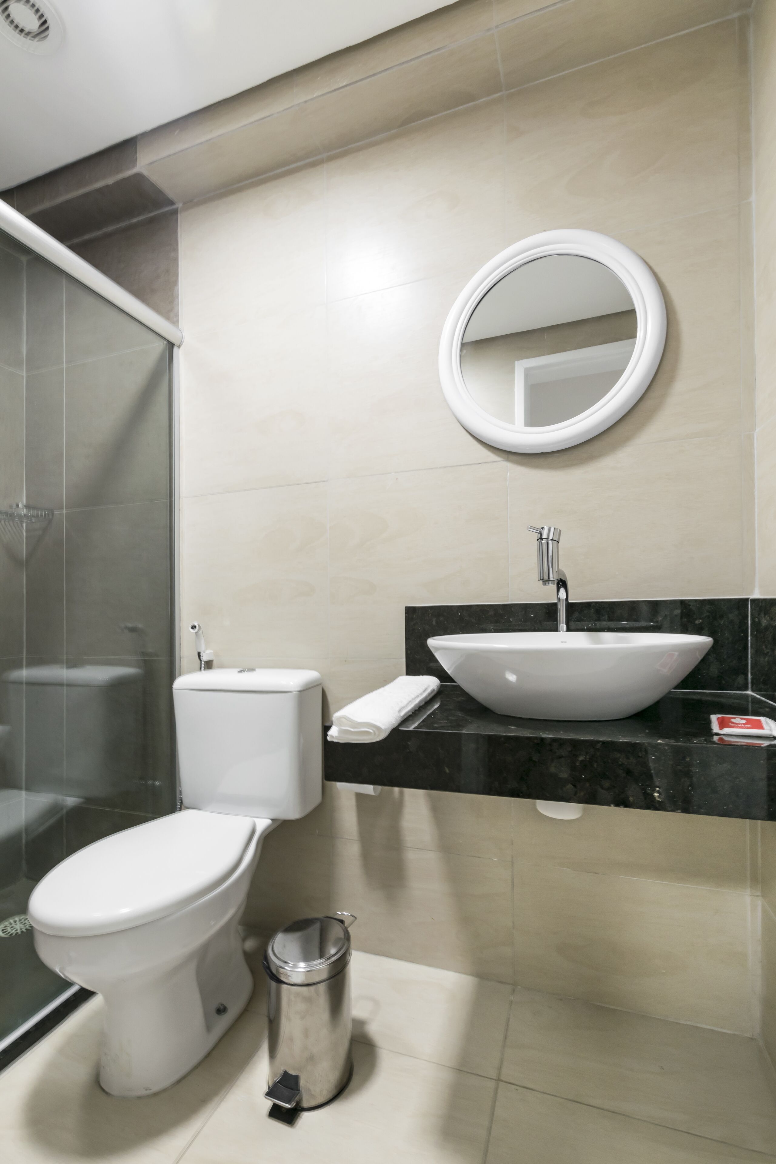 Un baño moderno con inodoro blanco, lavabo con espejo redondo y cabina de ducha con mampara de vidrio.