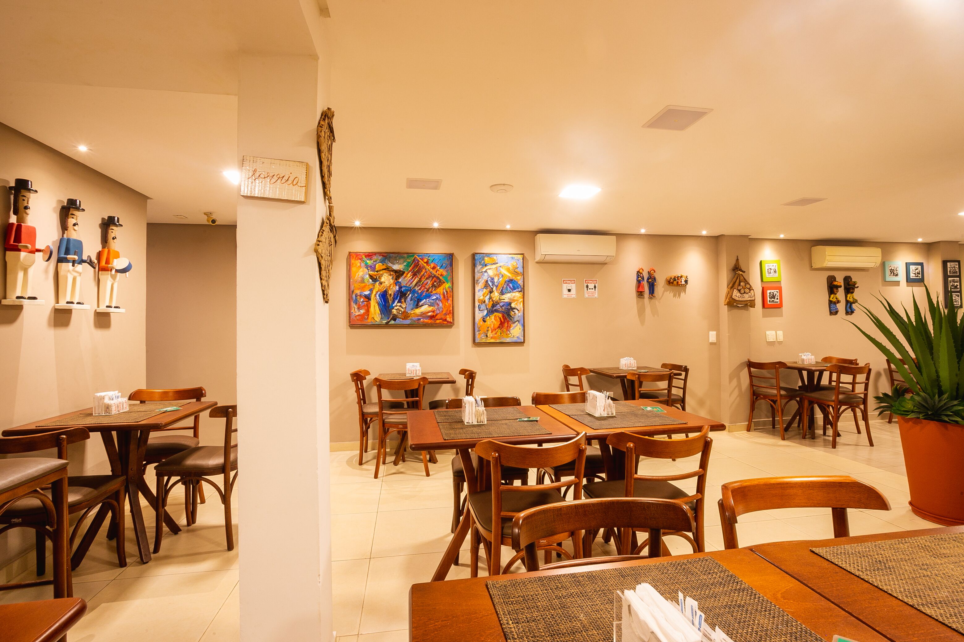 Un restaurant avec des tables et des chaises en bois, des œuvres d’art accrochées aux murs et une plante en pot.