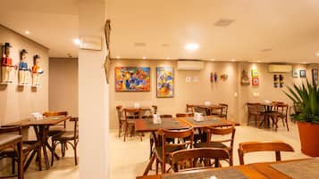 A restaurant with wooden tables and chairs, artwork on the walls, and a potted plant.