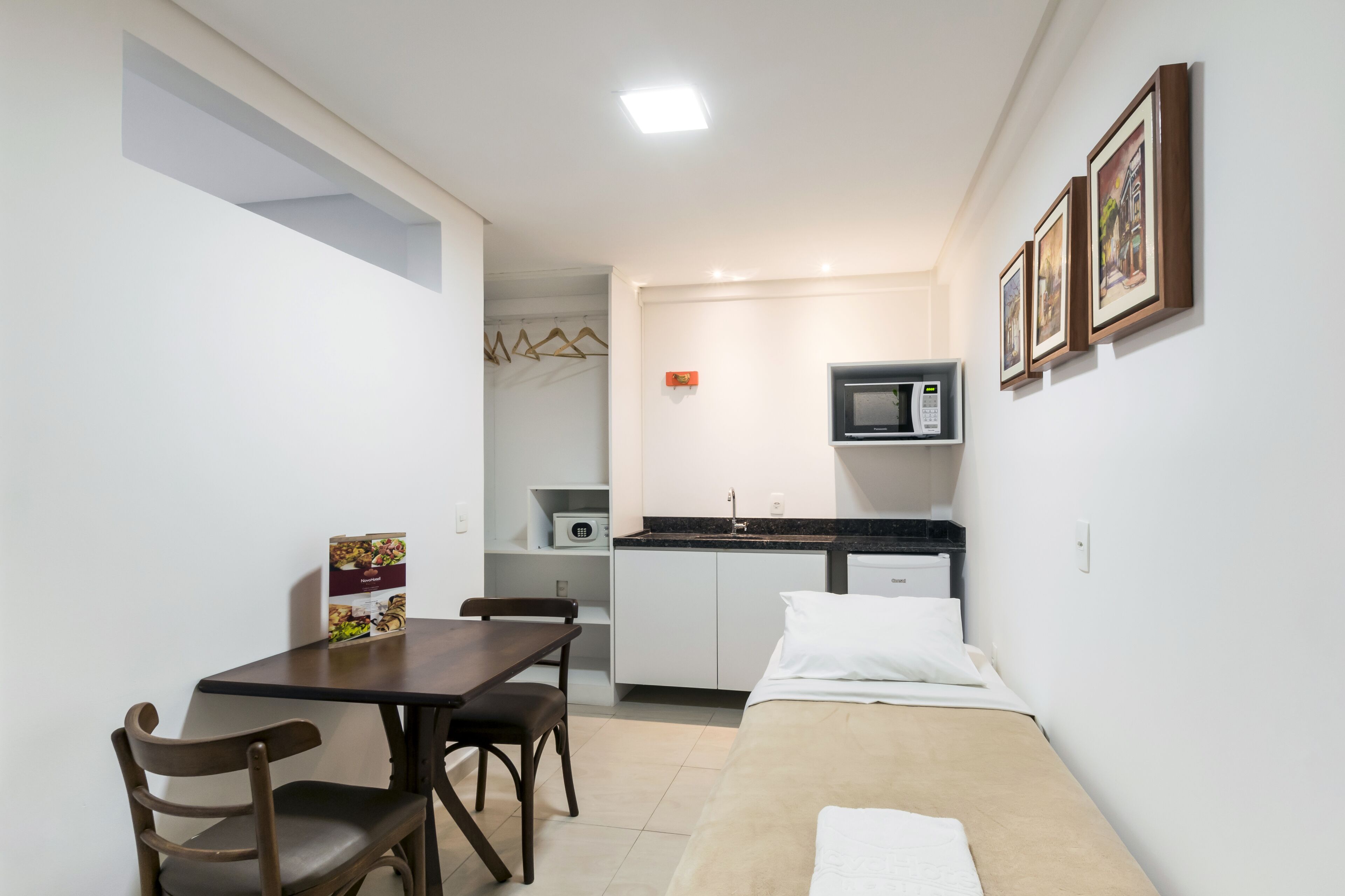 Quarto compacto com cama, uma mesa pequena com cadeiras, cozinha compacta e micro-ondas.