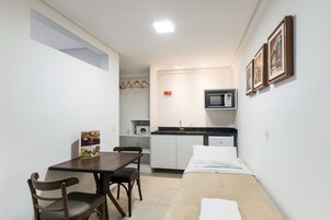 Una habitación compacta con cama, una pequeña mesa con sillas, kitchenette y microondas.