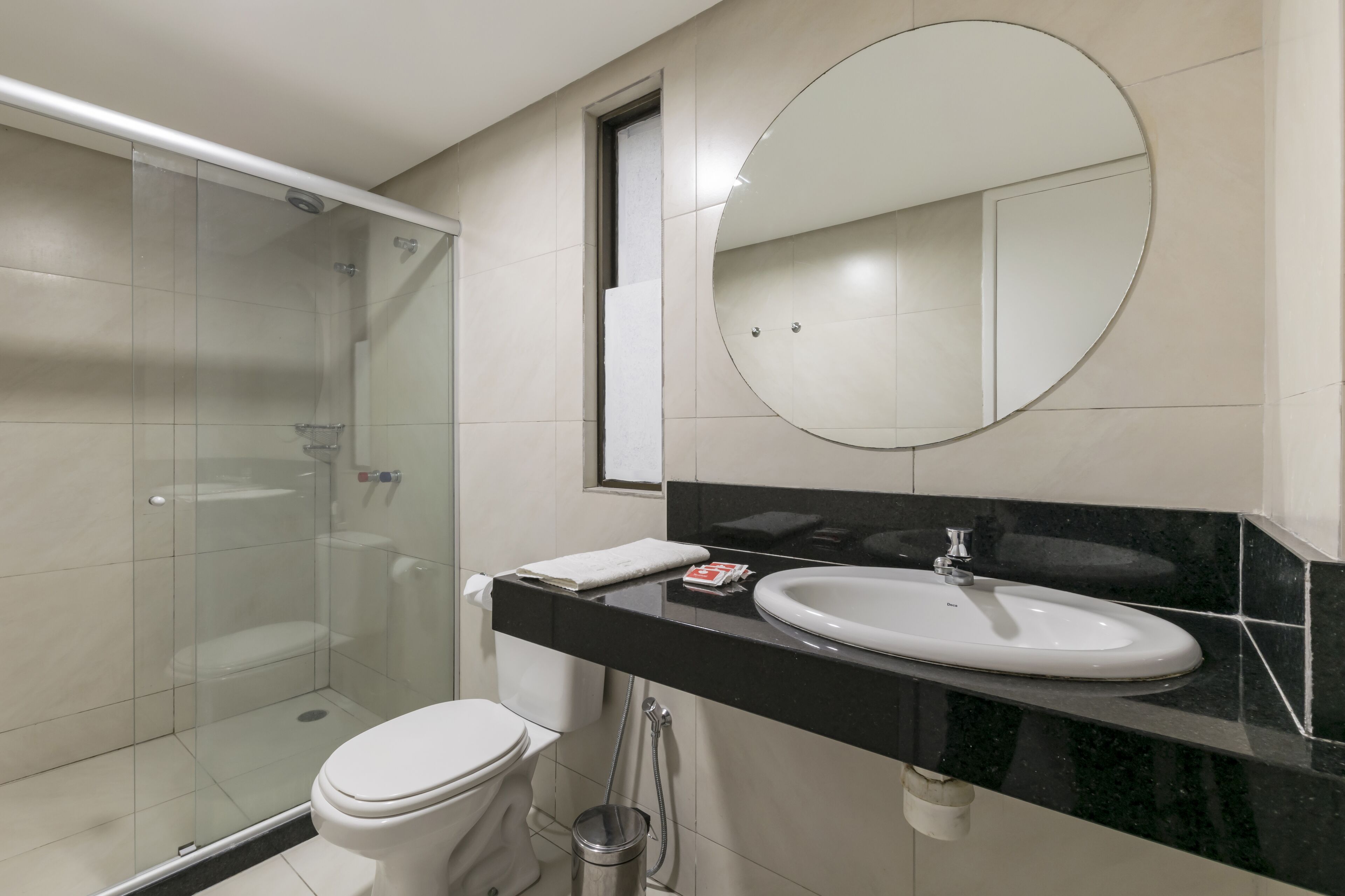 Een moderne badkamer met een glazen douchecabine, een wit toilet, een zwart aanrecht met een wastafel en een grote spiegel.