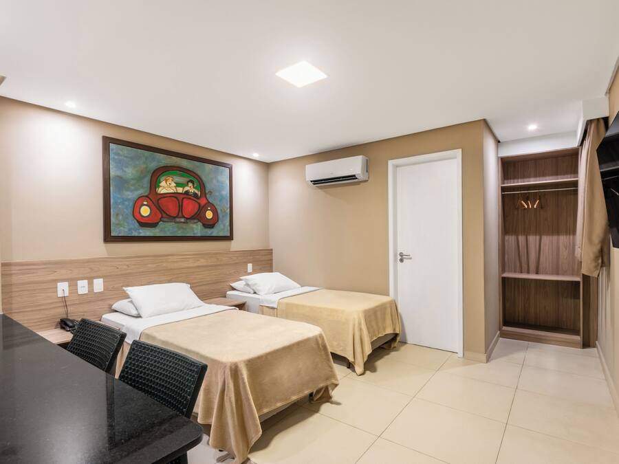 Quarto de hotel com duas camas, uma escrivaninha, televisão, ar condicionado e um guarda-roupa.