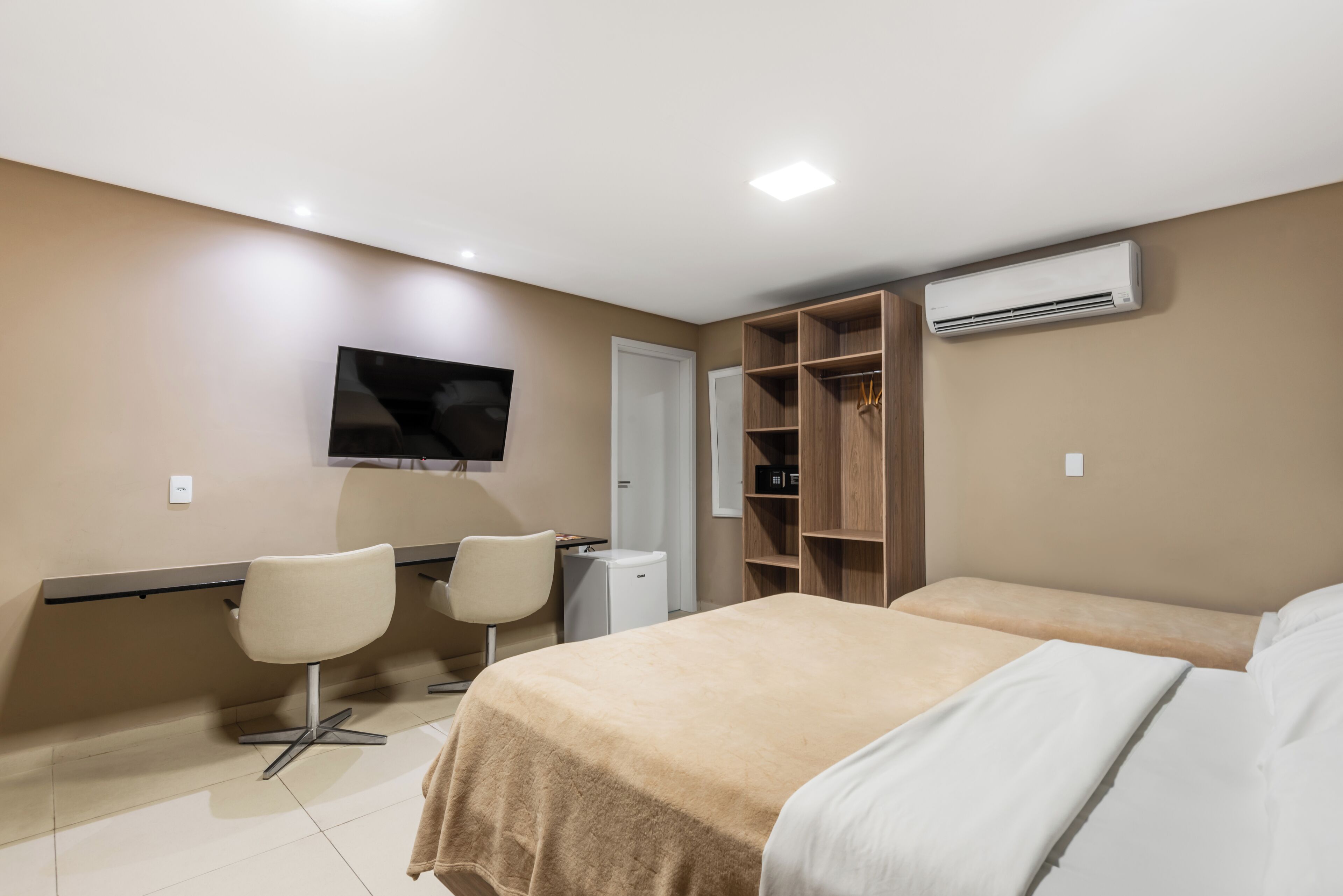 A hotel room with a bed, two chairs, a desk, a TV, and a wardrobe.