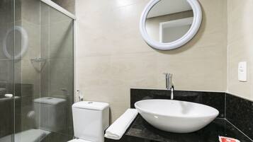 A modern bathroom with a glass shower enclosure, a white toilet, a sink with a black countertop, and a round mirror on the wall.