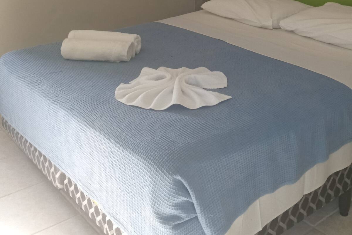 A neatly made bed with a blue and white bedspread, white pillows, and a folded towel on the side.