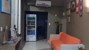A living room with a white sofa, a small yellow table, a refrigerator, and a wall with framed certificates. - Pousada Boi Bumbá Praia (João Pessoa)