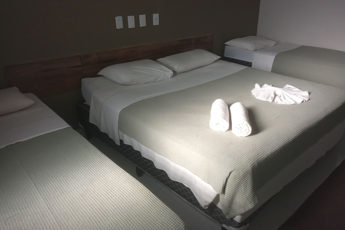 A hotel room with two beds, each with white linens and pillows. There are towels on the beds and a nightstand with a lamp.