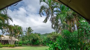 A view from a tented area overlooking a lush garden with palm trees and a grassy lawn. - Ikurangi Eco Retreat (Rarotonga)