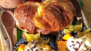 A tray with croissants, fruit, and two drinks with flowers. - Ikurangi Eco Retreat (Rarotonga)