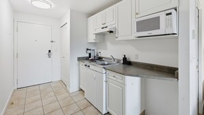 Uma cozinha compacta com armários brancos, micro-ondas embutido, pia e lava-louças.