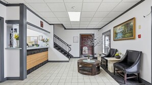 Uma área de recepção com balcão, escada, mesa de madeira redonda e uma cadeira de couro preto.