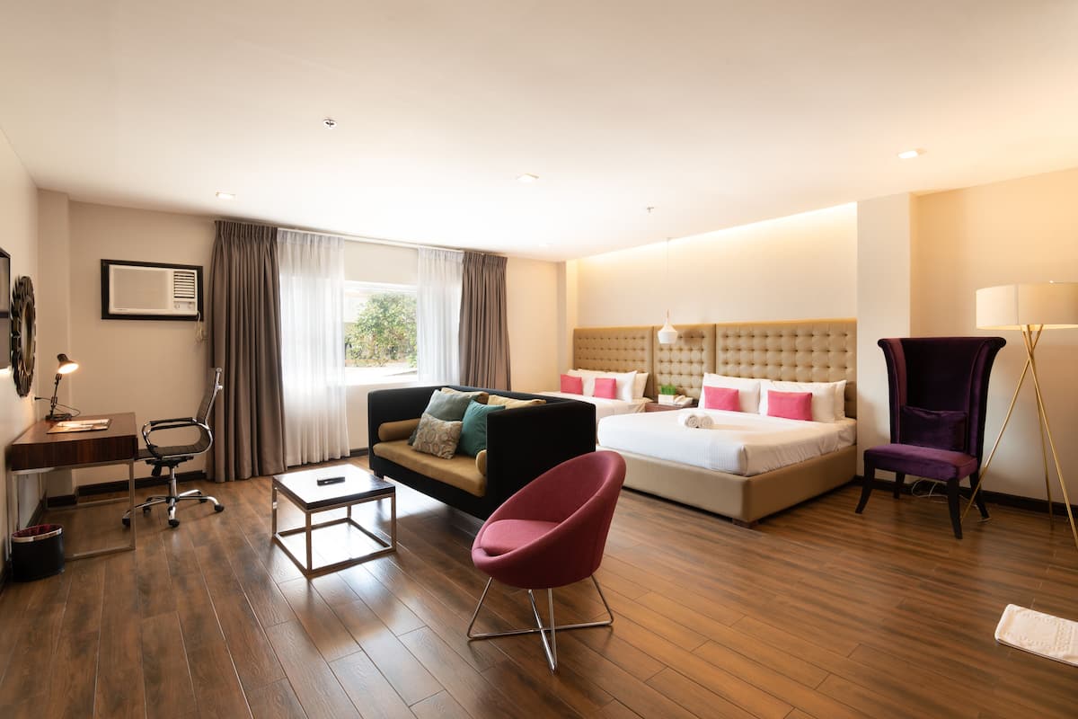 A hotel room with a bed, a sofa, a desk, a chair, and a window with curtains.