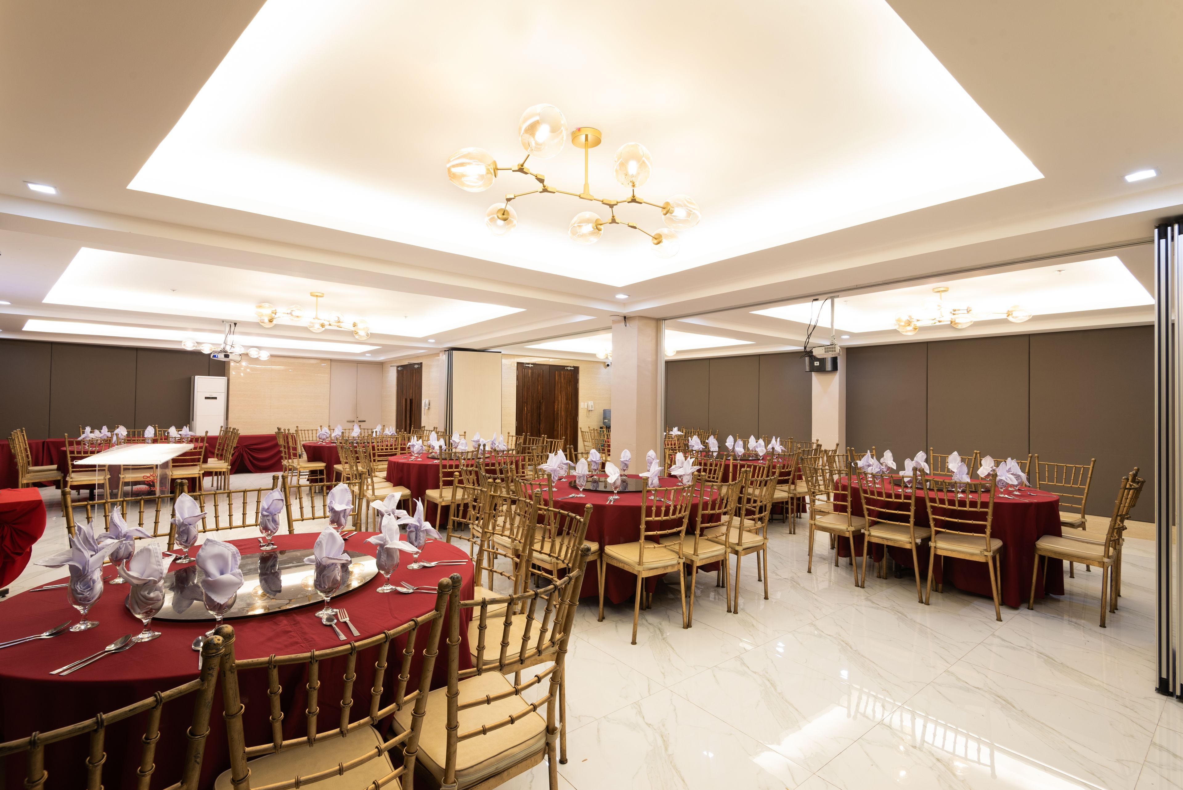 A banquet hall with round tables, chairs, and chandeliers.