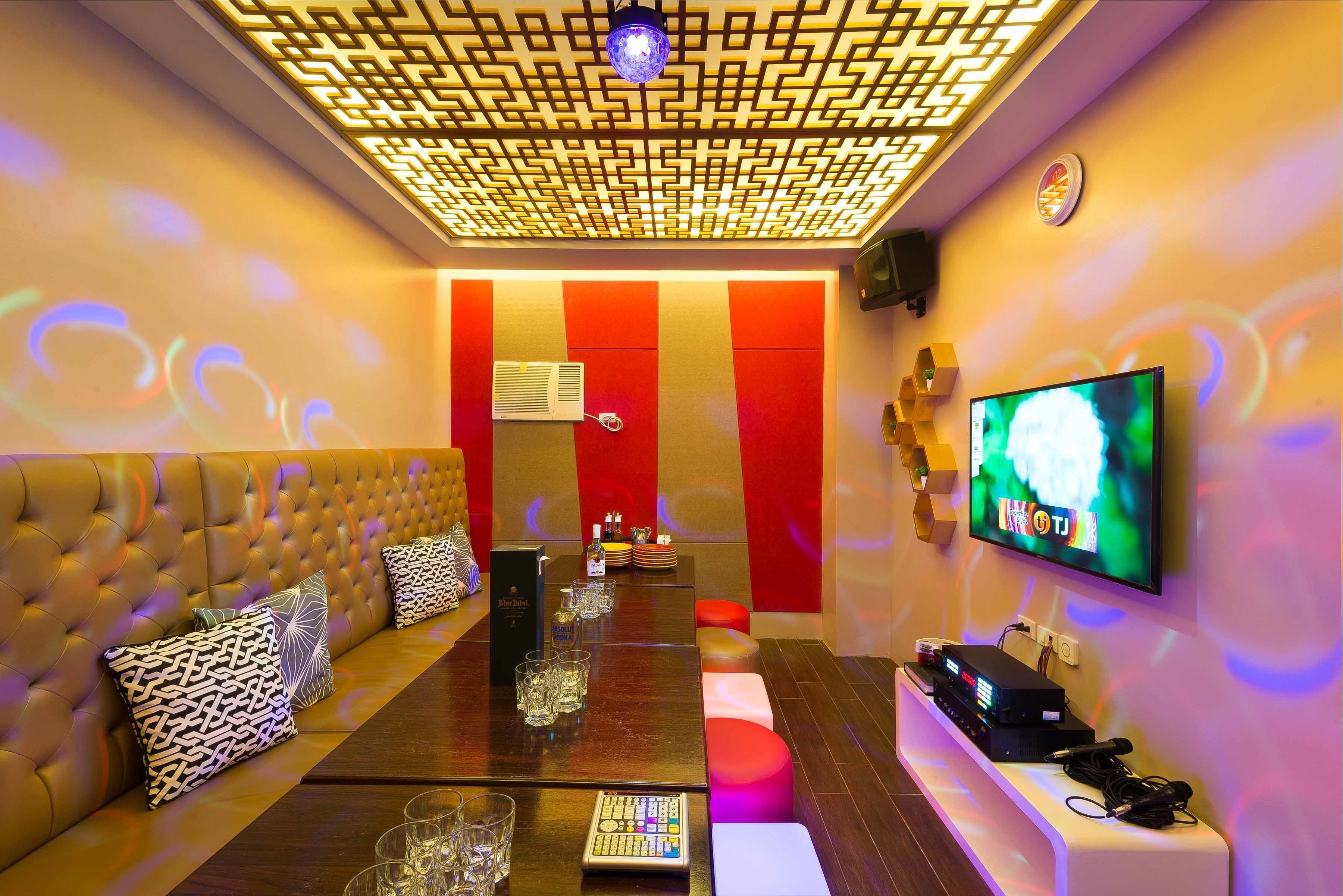 Een moderne zithoek met een gestoffeerde bank, een lange tafel met glazen, een flatscreen televisie en een plafond met een patroon.