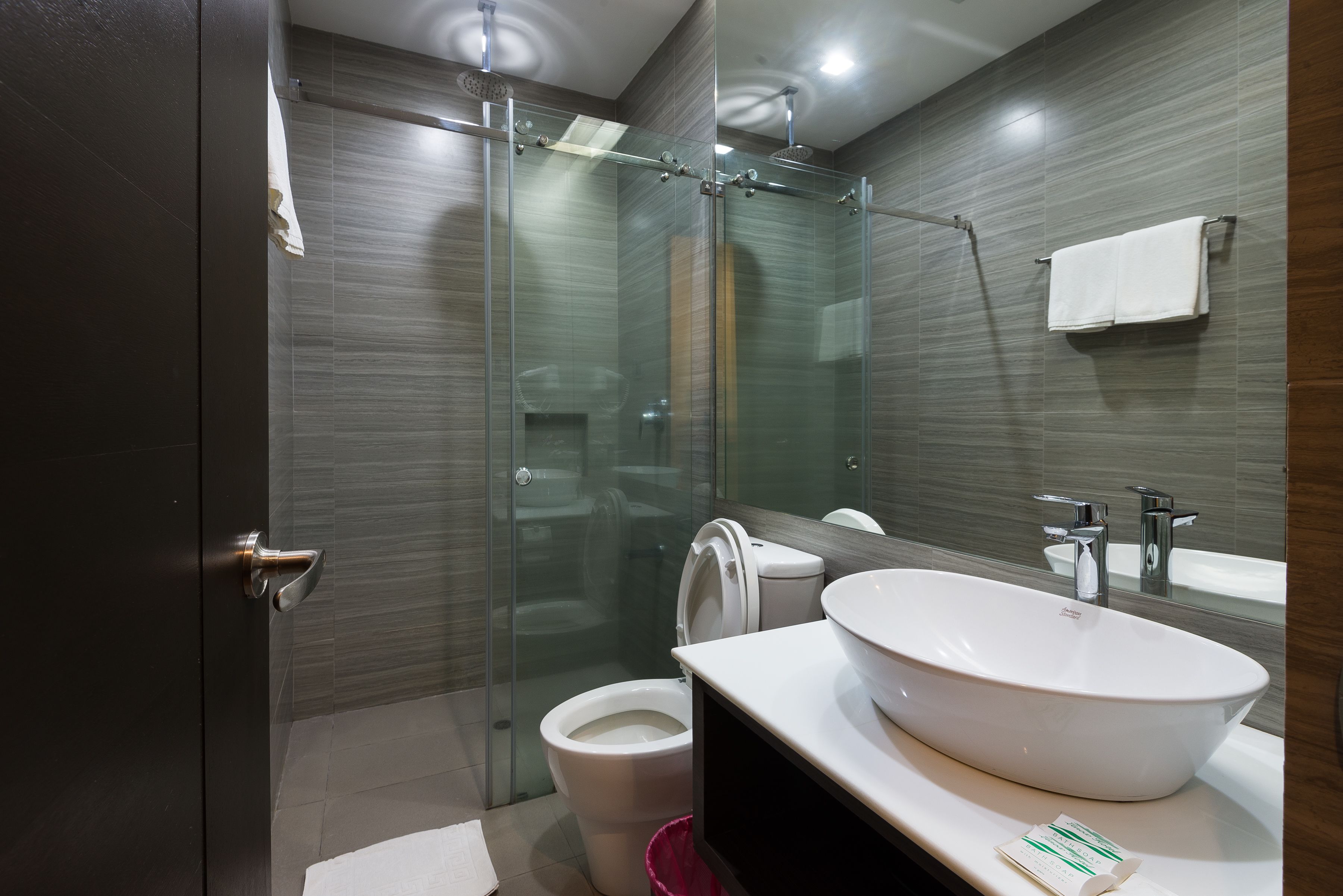 A modern bathroom with a glass-enclosed shower, a white toilet, and a large white sink with a mirror above it.
