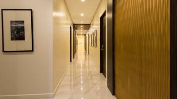 A hotel hallway with a polished marble floor, framed pictures on the walls, and a wooden panel on one side.