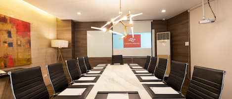 A conference room with a long table, black chairs, a projector screen, and a modern chandelier.