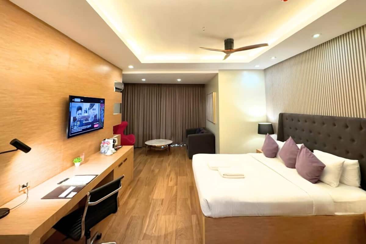 A hotel room with a bed, desk, TV, ceiling fan, and a small seating area.