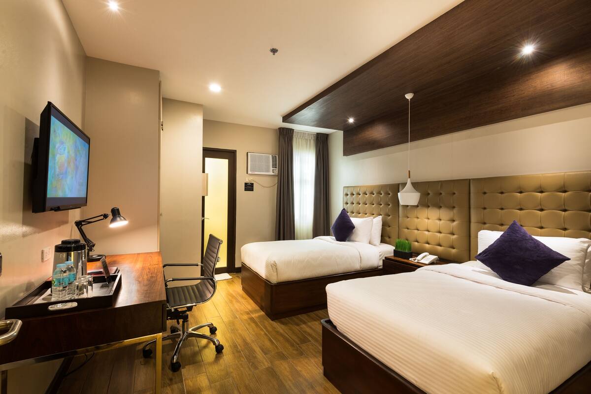 A hotel room with two beds, a desk with a computer, a chair, and a TV on the wall.