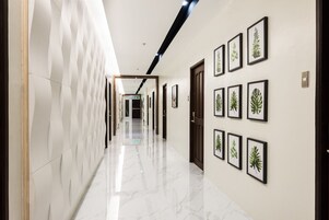 Um corredor com piso de mármore, quadros botânicos nas paredes e uma porta no final.